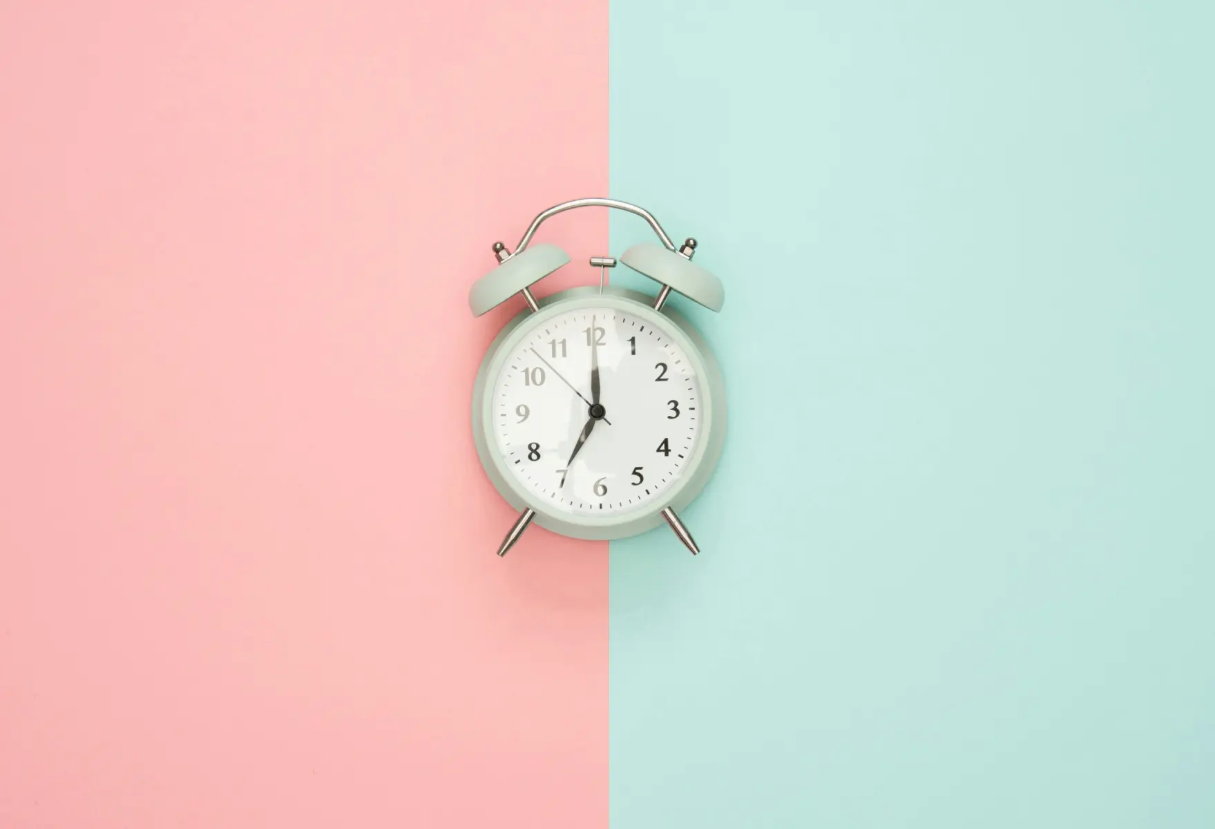 A close up image of an alarm clock on a background split in the middle with pink on the left and blue on the right